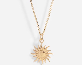 May include: A gold-toned necklace featuring a delicate chain and a sun-shaped pendant. The pendant has a smooth, circular center with radiating, tapered rays extending outward, creating a detailed sunburst design that hangs from a small jump ring.