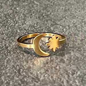 May include: A gold-colored ring featuring a crescent moon and a star design. The ring is made of a shiny metal and has a simple, elegant style. The celestial-themed ring is a fashionable accessory.