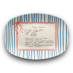 May include: Oval serving platter with a blue and white striped design. A handwritten recipe for "Cherry Surprise" is centered, framed in red, with a red bow. The recipe includes ingredients and instructions.