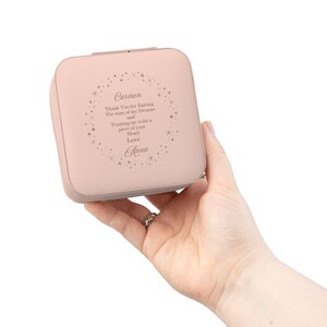 May include: A blush pink jewelry box with a square shape. The box has a lid and is held in a hand. The text on the box reads "Carmen, Thank You for Raising The man of my Dreams and Trusting me with a piece of your Heart Love Anna."