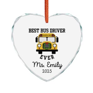 Op de afbeelding: Hartvormige ornament met de tekst "BEST BUS DRIVER EVER Ms. Emily 2025" en een gele schoolbusafbeelding. Het ornament is helder met een oranje lint om op te hangen.
