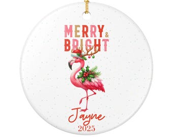 Może przedstawiać: Okrągła, biała ozdoba świąteczna z różowym flamingiem w czapce Świętego Mikołaja i rogami. Tekst brzmi "MERRY & BRIGHT" i imię "Jayne" z rokiem "2025".