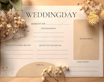 May include: A beige wedding day card with the text "WEDDINGDAY" at the top. The card has fill-in-the-blank sections with German phrases and a space for a photo. Dried flowers and leaves are arranged around the card.