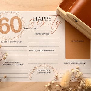 Könnte beinhalten: Geburtstagskarte mit dem Schriftzug "Happy Sixty" in Schreibschrift, mit der Zahl 60 in glitzerndem Gold. Die Karte enthält Aufforderungen zum Schreiben von Erinnerungen und Wünschen, mit einem Polaroid-Fotobereich.