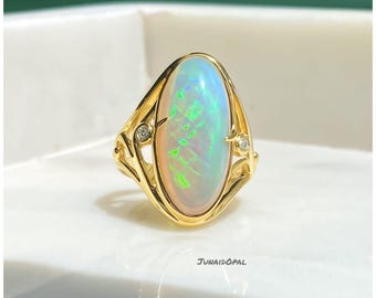 Könnte beinhalten: Ein goldener Ring mit einem ovalen Opal-Edelstein mit irisierenden Farben wie Grün, Blau und Rosa. Der Ring hat ein detailliertes Goldband mit kleinen Diamanten auf beiden Seiten des Opals.