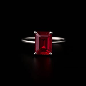 Könnte beinhalten: Ein silberner Ring mit einem großen, rechteckigen, tiefroten Edelstein. Der Edelstein ist der Mittelpunkt, vor einem schwarzen Hintergrund. Der Ring hat ein dünnes, poliertes Band mit vier Krappen, die den Stein sichern.