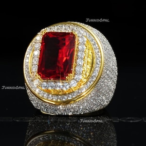 May include: A gold ring featuring a large rectangular red center stone surrounded by two concentric halos of small clear stones. The entire surface of the ring band is densely encrusted with tiny clear stones. The text JUNAIDOPAL is visible.
