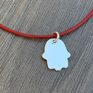 May include: A silver Hamsa hand charm pendant on a red leather cord.