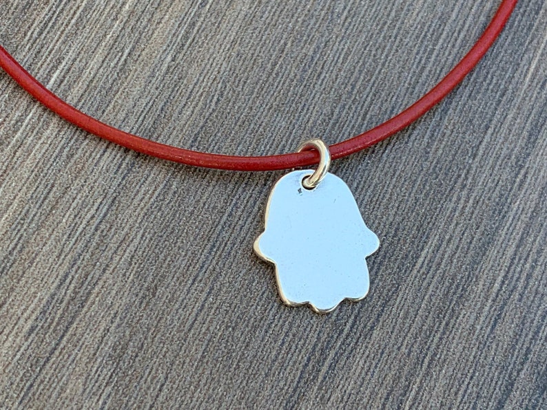 May include: A silver Hamsa hand charm pendant on a red leather cord.