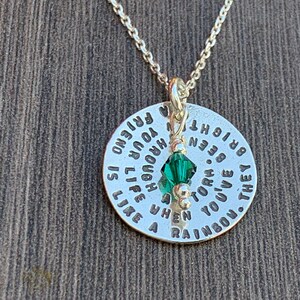 May include: Silver necklace with a round pendant that reads "They've  given you a rainbow when you've been torn by a storm. Life is like a laugh, you're enough to  brighten  your friend". A green crystal charm hangs from the pendant.