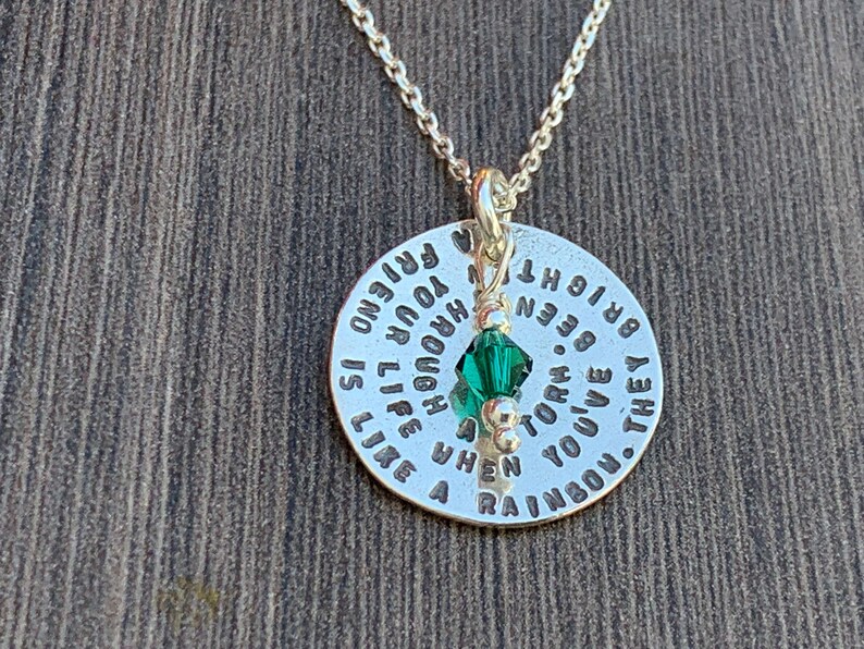May include: Silver necklace with a round pendant that reads "They've  given you a rainbow when you've been torn by a storm. Life is like a laugh, you're enough to  brighten  your friend". A green crystal charm hangs from the pendant.