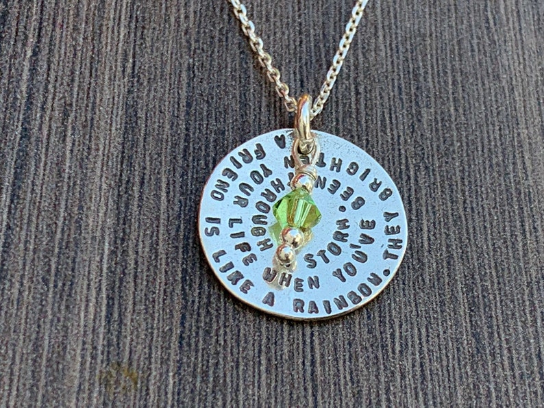May include: Silver necklace with a round pendant that reads "They've been through a storm. When you've been through a storm, life is like a rainbow. You're a friend." The pendant has a green crystal charm.