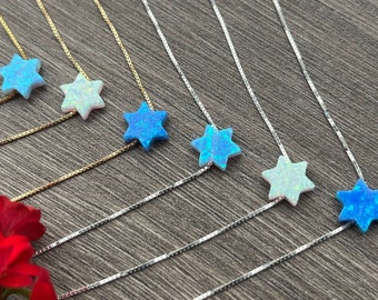 May include: A collection of six necklaces featuring star-shaped pendants. Three necklaces have gold-toned box chains, and three have silver-toned box chains. The pendants are made of iridescent opal-like material in shades of blue and white.
