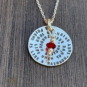 May include: Silver necklace with a round pendant that reads "They say you've been through a storm. When you live through your rainbow is like a friend to you". A red crystal hangs from the pendant.