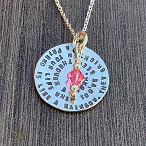 May include: A silver necklace with a round pendant that reads "A friend is like a rainbow. They brighten your life though the hard times." The pendant has a pink crystal charm.