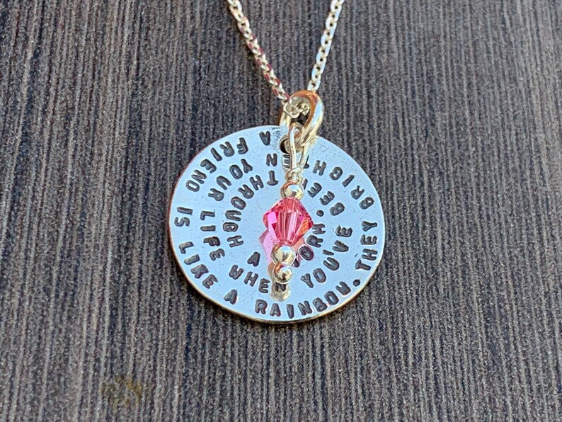 May include: A silver necklace with a round pendant that reads "A friend is like a rainbow. They brighten your life though the hard times." The pendant has a pink crystal charm.