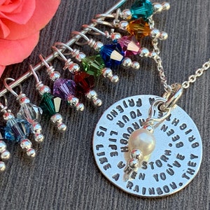 May include: A silver necklace with a charm that reads "A friend is like a rainbow. They brighten your life through every storm. When you've been through a storm, you give a rainbow." The charm is attached to a silver chain with a pearl bead. The necklace also has a silver bar with colorful crystal beads hanging from it.