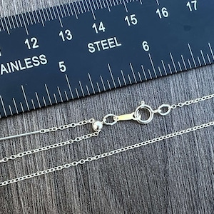 Puede incluir: Un collar de cadena de plata con un cierre de langosta y una pequeña perla de plata. La cadena mide 17 pulgadas (43 cm) de largo y se mide con una regla que dice "Acero inoxidable".