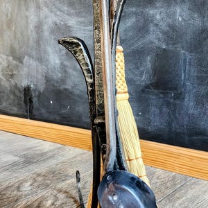 May include: A black metal fireplace tool set with a broom, shovel, and poker. The tools are attached to a stand that resembles a tree branch.