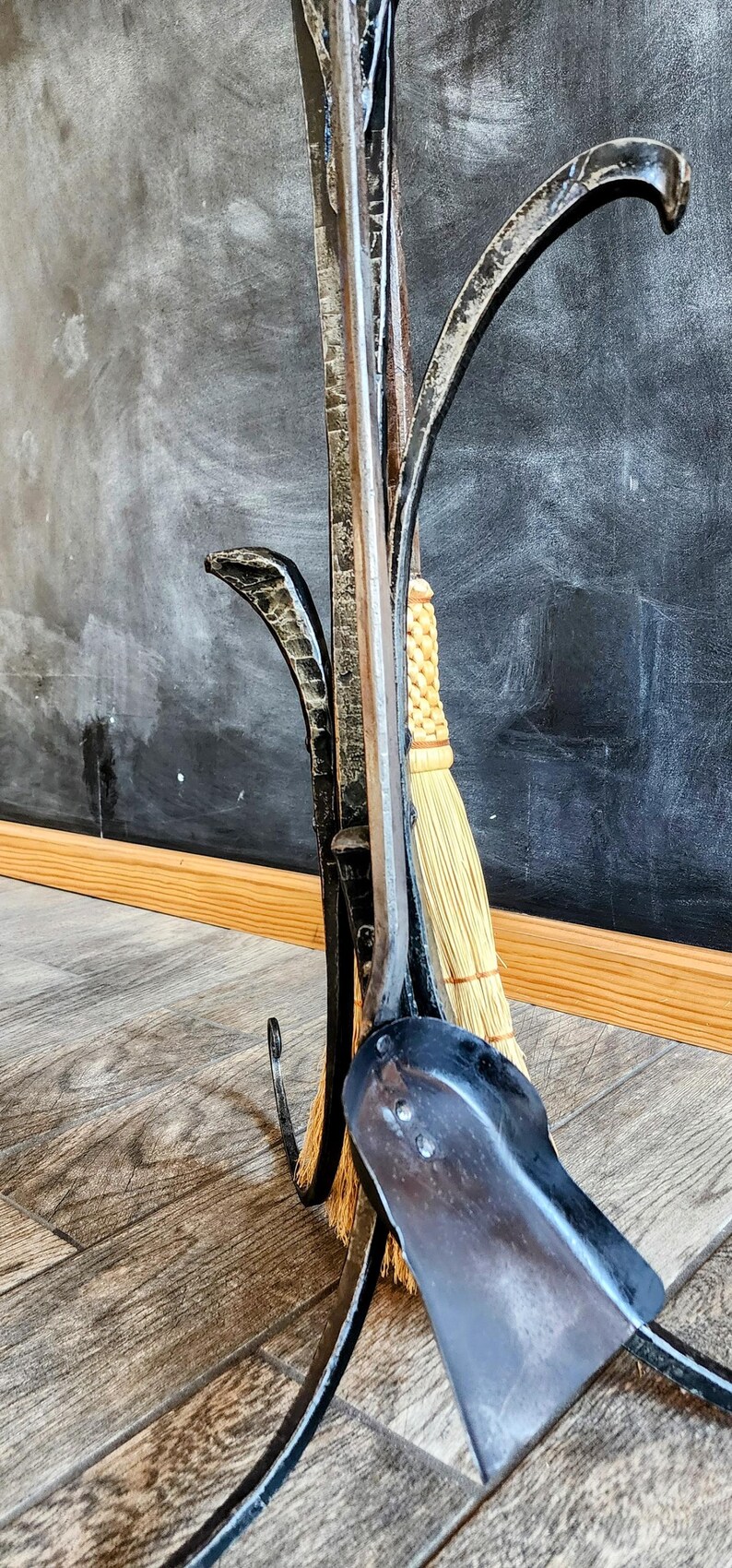 May include: A black metal fireplace tool set with a broom, shovel, and poker. The tools are attached to a stand that resembles a tree branch.