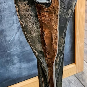 May include: A metal sculpture of a stylized plant with a copper-colored stem and black metal leaves. The sculpture has a rustic, hand-forged look.