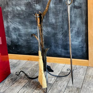 May include: A black metal fireplace tool holder with a curved top and three legs. A long-handled brush and two metal tools are hanging from the holder.