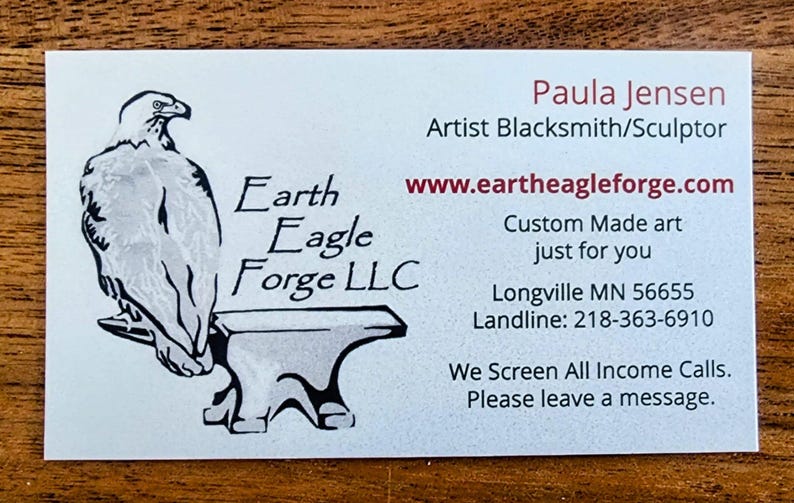 May include: A business card for Earth Eagle Forge LLC, a blacksmith and sculptor. The card features a black and white illustration of an eagle perched on an anvil. The text on the card reads "Paula Jensen, Artist Blacksmith/Sculptor, www.eartheagleforge.com, Custom Made art just for you, Longville MN 56655, Landline: 218-363-6910, We Screen All Income Calls. Please leave a message."