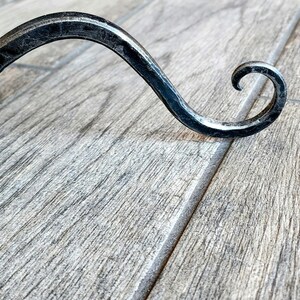 May include: A black metal hook with a curved design. The hook is made of wrought iron and has a rustic finish.