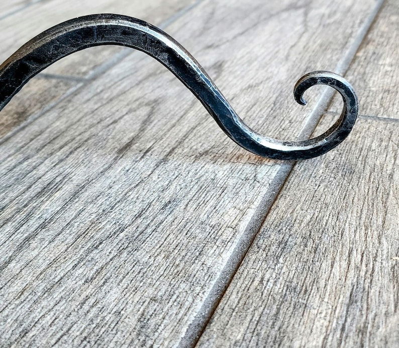 May include: A black metal hook with a curved design. The hook is made of wrought iron and has a rustic finish.