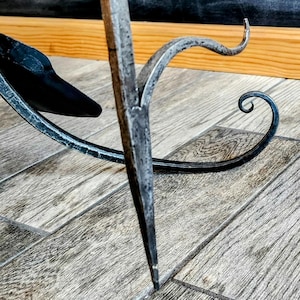May include: A black metal stand with a decorative scroll design. The stand has a pointed base and a curved top.