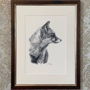 Könnte beinhalten: Eine Kohlezeichnung eines Fuchses im Profil, in Schwarz-Weiß auf weißem Papier ausgeführt. Das Kunstwerk befindet sich in einem dunkelbraunen Holzrahmen mit goldener Innenkante und einem weißen Passepartout. Eine Signatur ist unten rechts sichtbar.