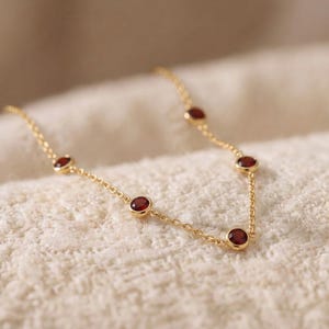 Op de afbeelding: Een delicate gouden ketting met vijf gelijkmatig verdeelde, ronde, dieprode granaat edelstenen in gepolijste gouden zettingen. De ketting is opgebouwd uit een fijne schakelketting die elk van de ronde steenzettingen met elkaar verbindt.