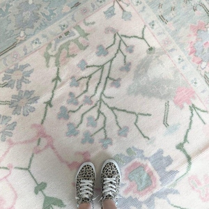 May include: Overhead view of two floral patterned rugs in pastel colors. The rugs feature a cream background with pink, blue, and green floral designs. A pair of leopard print sneakers are visible at the bottom of the image.