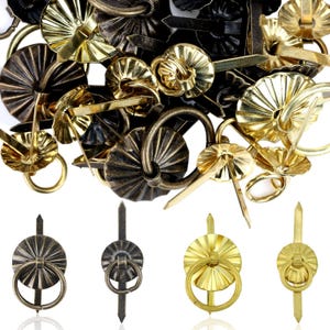May include: An assortment of antique brass and gold-toned decorative tacks and ring pulls. The tacks have a variety of ornate designs, including fluted and circular patterns. The ring pulls feature a circular ring attached to a decorative base.