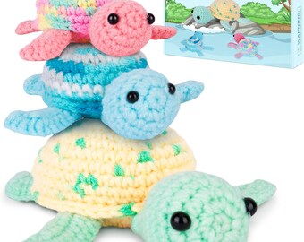 May include: A stack of four colorful, crocheted turtle toys. The turtles are in shades of pink, blue, yellow, and green. The turtles have black eyes and are stacked on top of each other. A box with a turtle illustration is in the background.