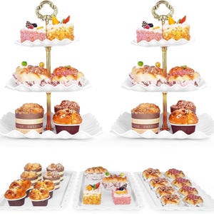May include: A white, three-tiered serving stand with gold detailing, laden with cakes and pastries. The stand has a decorative handle and scalloped edges. The pastries include cupcakes, mini cakes, and other baked goods, ideal for a dessert display.