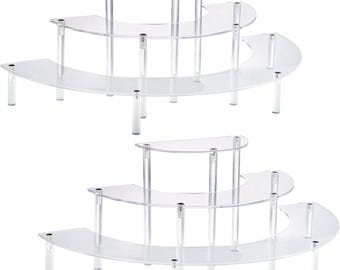 May include: Two clear acrylic display stands. Each stand has three curved tiers and a half-circle top tier. The tiers are supported by clear cylindrical legs. The stands are designed to showcase items.