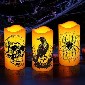 Pode incluir: Três velas LED com tema de Halloween com brilho laranja e amarelo. Uma vela apresenta uma caveira, outra um corvo em uma abóbora e a terceira uma aranha em uma teia. As velas são cilíndricas.