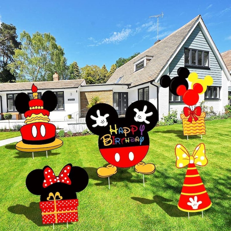 May include: Colorful yard decorations featuring Mickey Mouse and Minnie Mouse designs. Includes a birthday cake, gift boxes, balloons, and a cone-shaped party hat. The decorations are set up on a green lawn in front of a house.