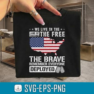 May include: Black t-shirt with a patriotic design. The shirt features the text "WE LIVE IN THE LAND OF THE FREE BECAUSE OF THE BRAVE" with an American flag graphic and military dog tags. The shirt is a tribute to the military.