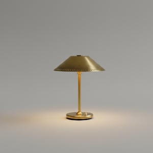 May include: A brass table lamp with a conical shade and a slender stem. The lamp has a circular base and is illuminated, casting a warm glow. The shade has a series of small perforations around the edge.