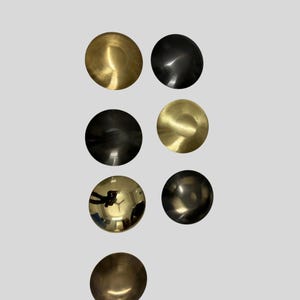 以下が含まれることがあります： 金と黒の色合いの7つの金属製の円形オブジェクトが、明るい灰色の背景に配置されています。 オブジェクトは光を反射し、ハイライトと影を作り出しています。 オブジェクトは金属で作られているようです。