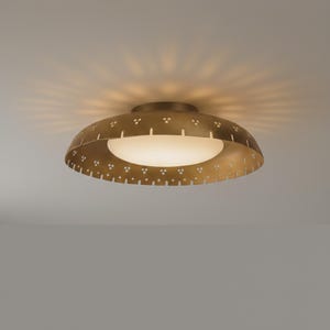 May include: A brass-colored, mid-century modern ceiling light fixture. The fixture has a rounded, perforated shade with a white, circular light source. The light casts a pattern on the ceiling.