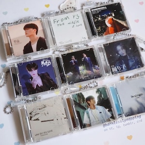 Puede incluir: Una colección de llaveros transparentes con forma de CD. Cada llavero presenta una imagen de portada de álbum diferente, con imágenes de músicos y texto, incluyendo "From rs the middle of June", "BAD" y "WONDERWALL".