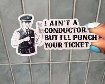 Puede incluir: Una pegatina troquelada que muestra a un revisor con chaleco y gorra oscuros sosteniendo un billete. La pegatina tiene un patrón de estrellas holográficas y el texto negro: I AIN'T A CONDUCTOR, BUT I'LL PUNCH YOUR TICKET. Borde blanco.