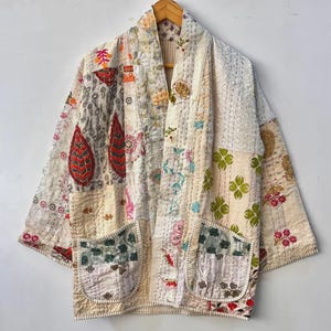 Peut inclure: Kimono patchwork crème avec divers patchs de tissu brodés et appliqués. La veste a deux poches avant et une coupe ample. Les patchs présentent des motifs floraux, cachemire et géométriques dans des tons de rouge, vert et bleu.