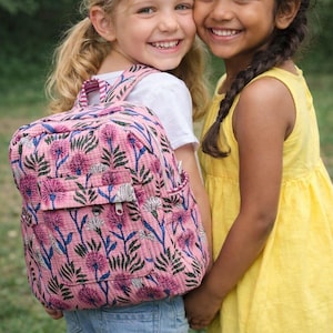 Peut inclure: Deux jeunes filles souriantes s'embrassent, l'une portant un sac à dos rose à motifs floraux. Le sac à dos présente un motif répété de fleurs roses et de feuilles vertes. L'autre fille porte une robe jaune. Les deux filles regardent l'appareil photo.