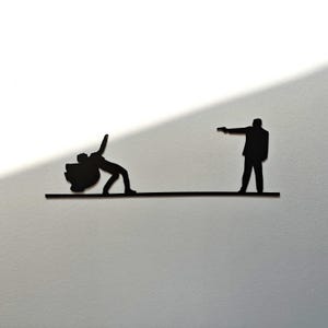 Peut inclure: Une œuvre d'art murale en métal noir représentant une scène dramatique. Une silhouette tombe, tandis qu'une autre se tient avec une arme pointée. Les personnages sont reliés par une ligne horizontale, créant une tension.