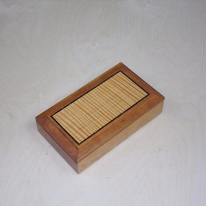 May include: A rectangular wooden box with a light wood inlay and a dark wood border. The box has a smooth, polished finish.