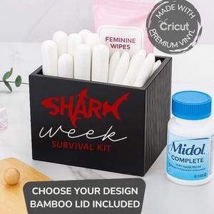 May include: A black box labeled "Shark Week Survival Kit" with white tampons, feminine wipes, and a bottle of Midol. A bamboo lid is included. The box has a red shark graphic and the text "Choose Your Design".